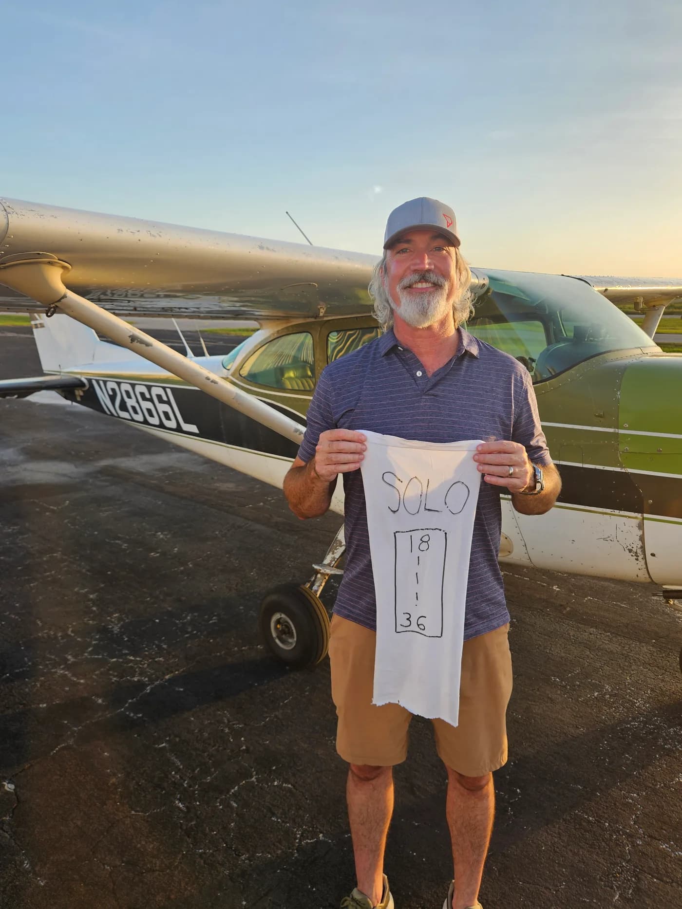 A Chapman Flight Academy student holds a marked shirttail after a first solo flight, standing in front of the Cessna 172H